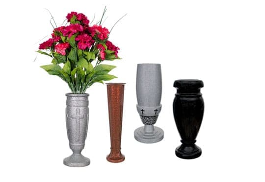 Four upright cemetery vases in granite and bronze finishes, one holding red silk flowers